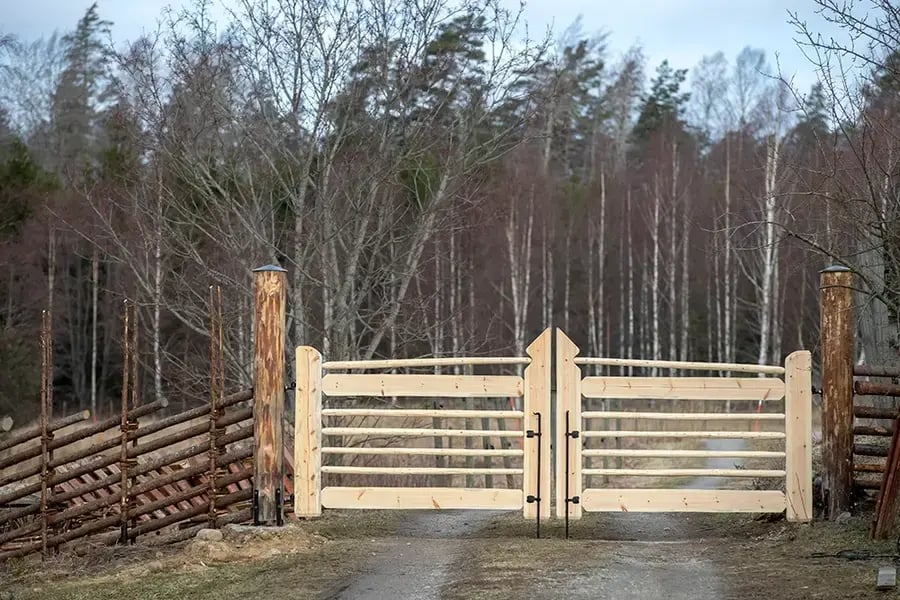 En närbild av en ny, ljus trägrind med svarta gångjärn och två robusta stockstolpar.