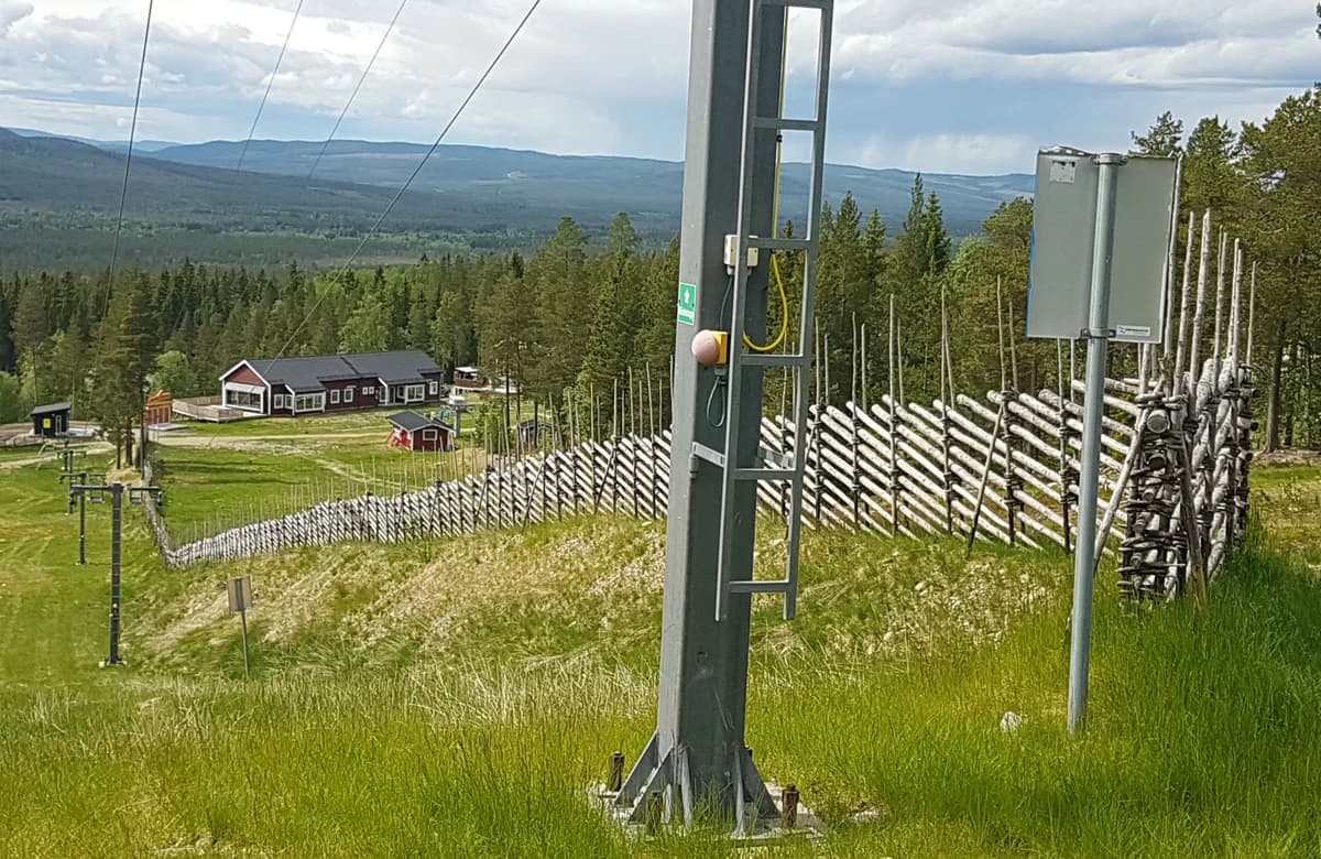 Traditionell gärdesgård längs skidbacke i Björnrike, med lift, fjällutsikt och skog i bakgrunden.